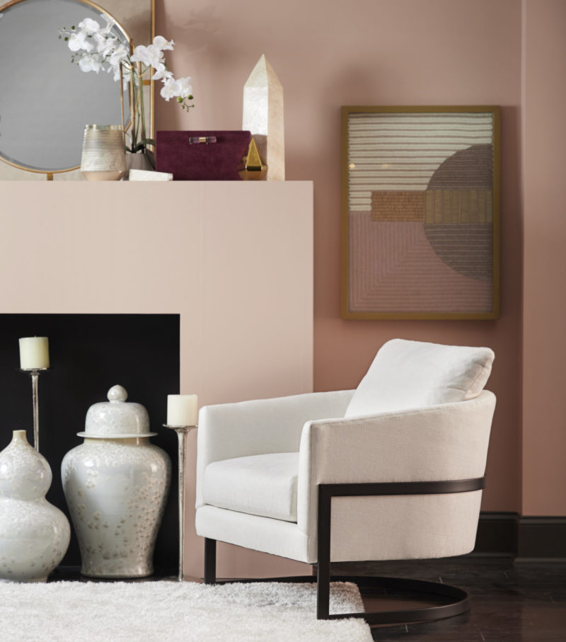 A minimalist/industrial style chair sits in front of modernist artwork on a dusty pink wall