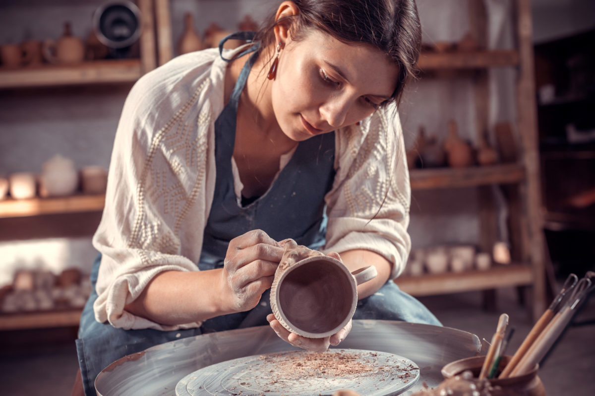 Stylish artisan making pottery, sculptor from wet clay on wheel. Craft manufacture.