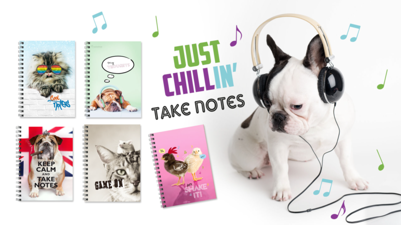 A french bulldog in headphones listens to music next to notebooks with cute animals on them